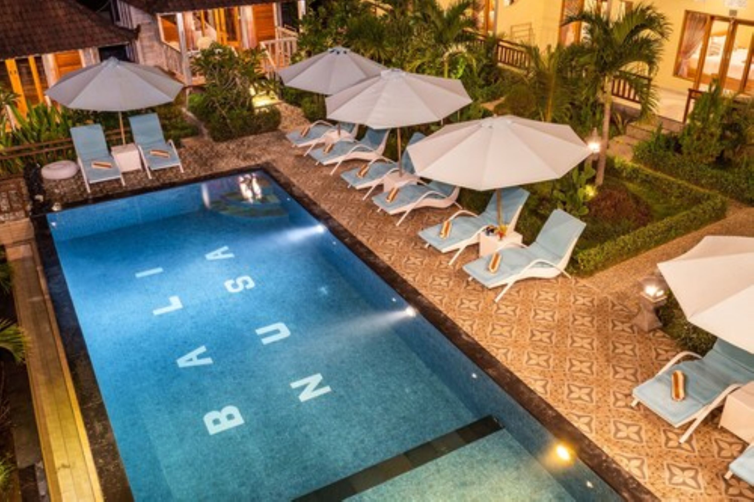 A swimming pool with lounge chairs and umbrellas, surrounded by greenery and a patterned walkway.