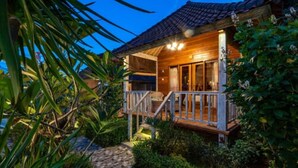 Une cabane en bois dotée d’un porche, entourée d’une végétation luxuriante et bordée d’un sentier en pierre.