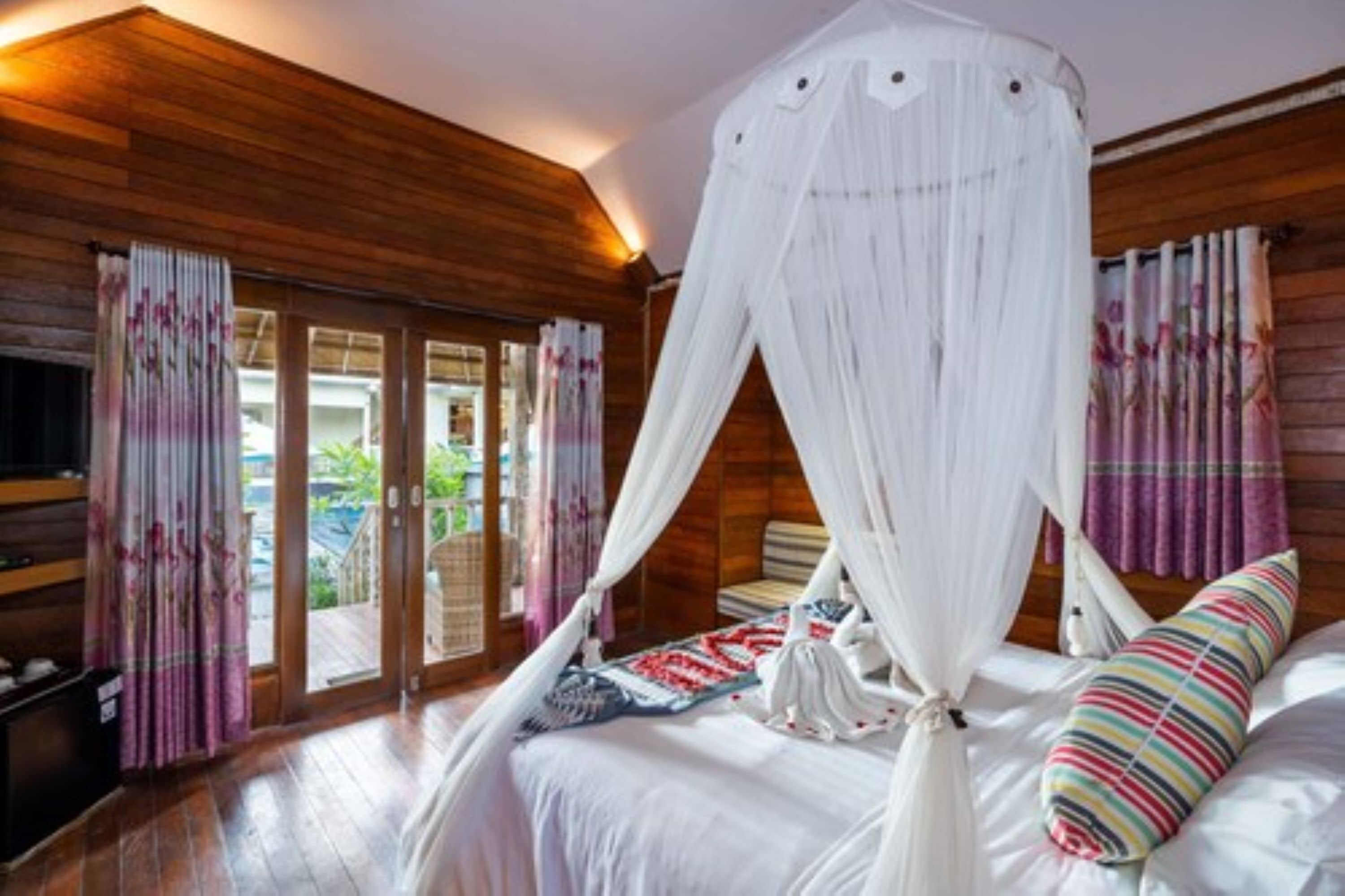 A bedroom with a canopy bed, wooden walls, and a view through the glass doors.
