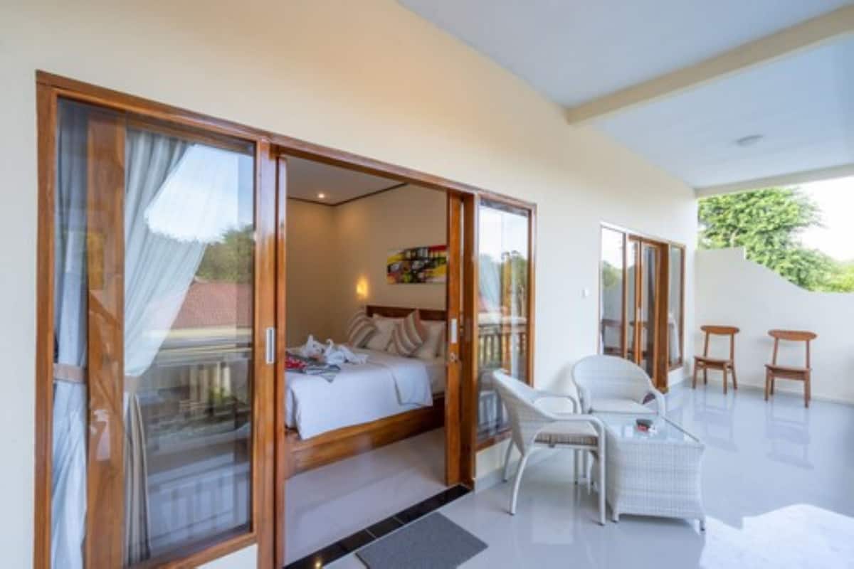 Ein Schlafzimmer mit Bett, Schreibtisch und Stuhl, sowie ein Balkon mit Blick ins Grüne.