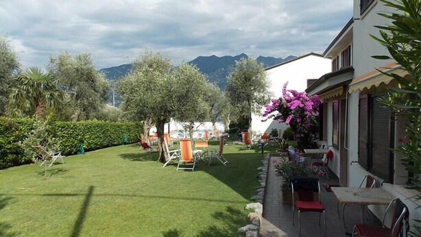 A well-maintained lawn with outdoor furniture, a stone pathway, and a view of mountains in the background. - Residence Alesi (Malcesine)