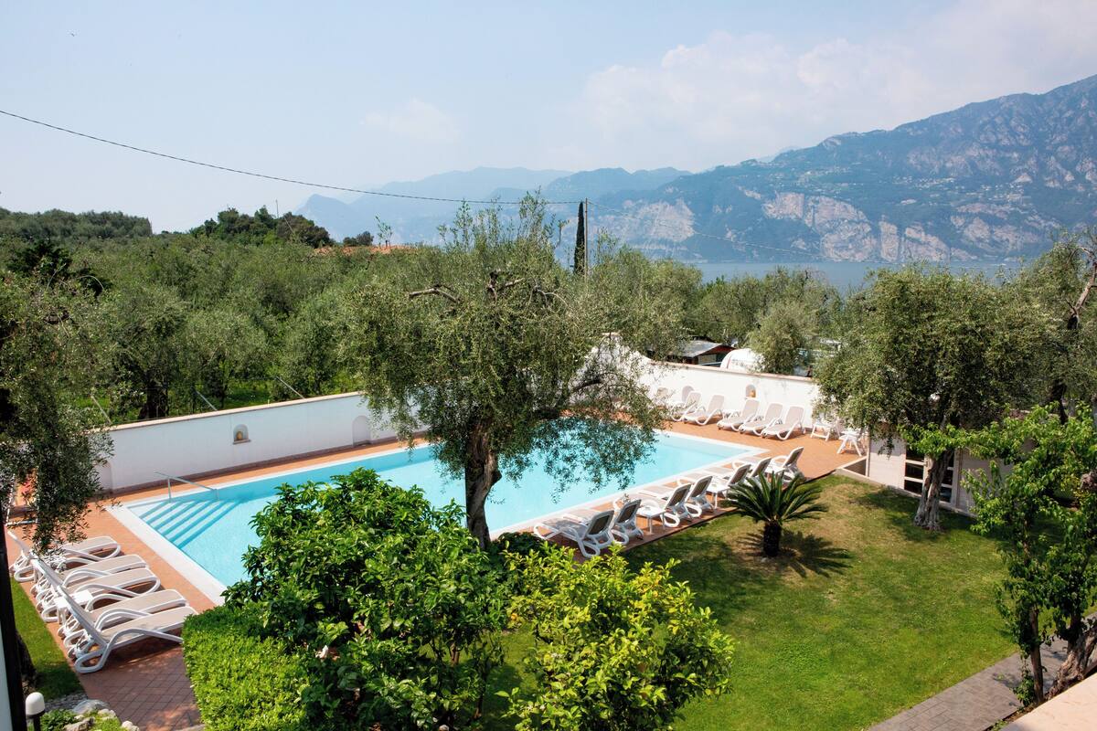 A swimming pool with lounge chairs, surrounded by greenery and mountains in the background.