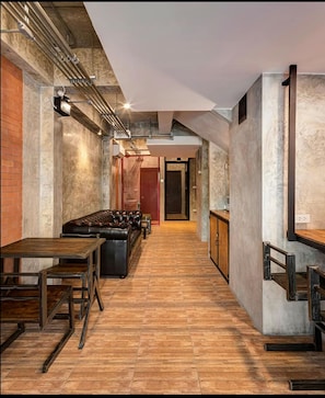 A narrow hallway with a wooden floor, a leather sofa, and a dining table with chairs. There are exposed pipes and a brick wall on one side. - The Step Chiang Mai - Adults Only (Chiang Mai)