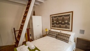 A neatly made bed with white linens and a green bedspread, a wooden ladder, a white wardrobe, and a framed artwork on the wall. - Romantic Maisonette (Chania)