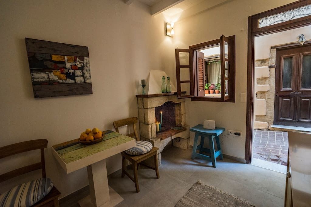 A cozy room with a dining table, chairs, a fireplace, and a window with an open shutter.
