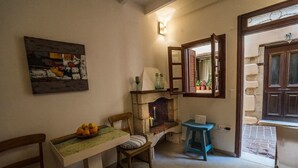 A cozy room with a dining table, chairs, a fireplace, and a window with an open shutter. - Romantic Maisonette (Chania)