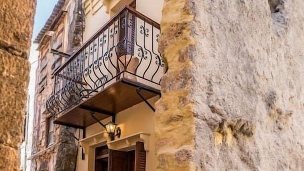 A narrow street with a building featuring a balcony with ornate metal railings. - Romantic Maisonette (Chania)