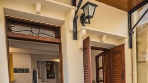 A narrow entrance with a wooden door, a small step leading into a room with a yellow cabinet, a white wall with a window, and a small white structure resembling a house. - Romantic Maisonette (Chania)