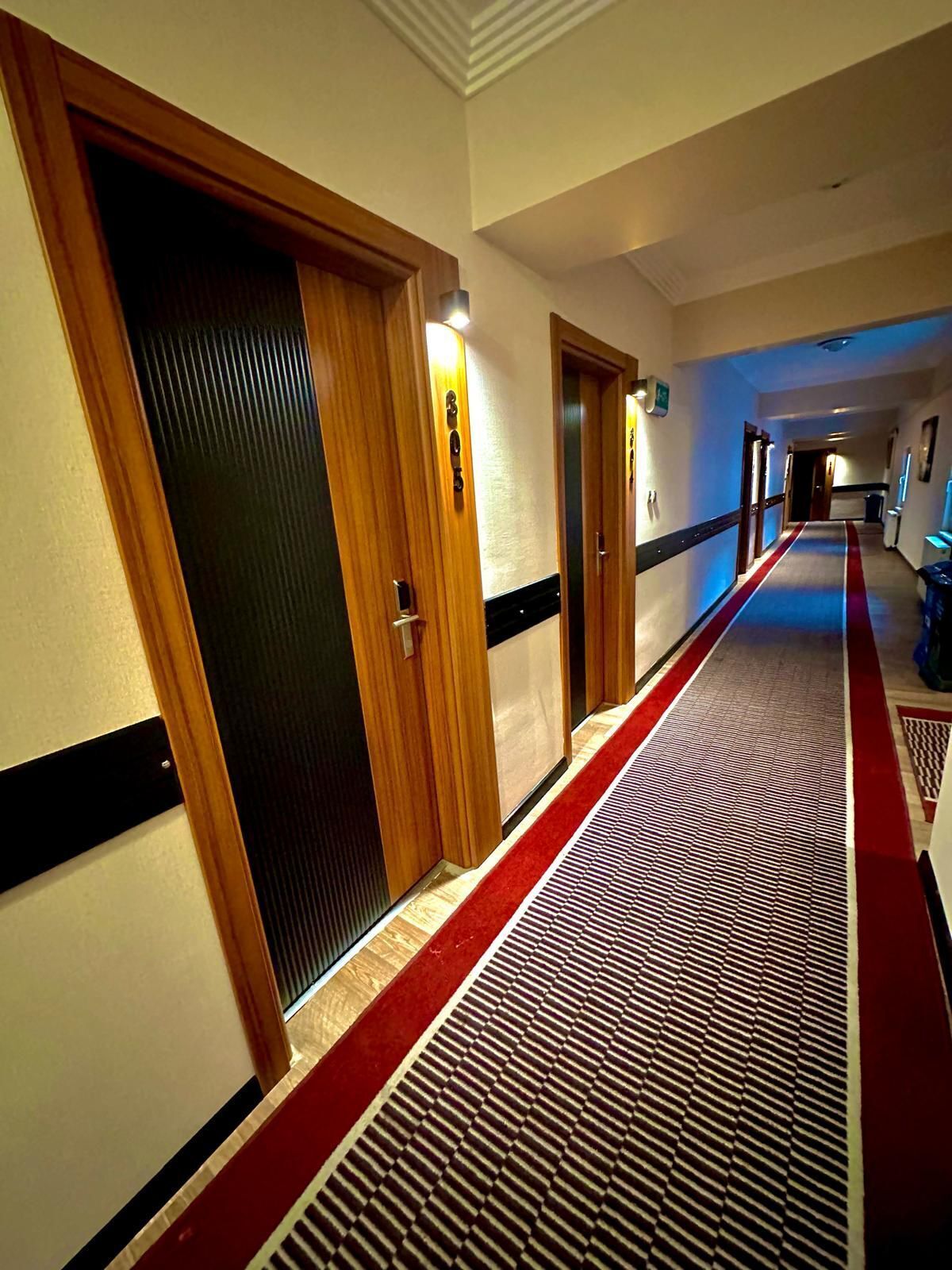 A hotel hallway with wooden doors, a red carpet, and a patterned floor.