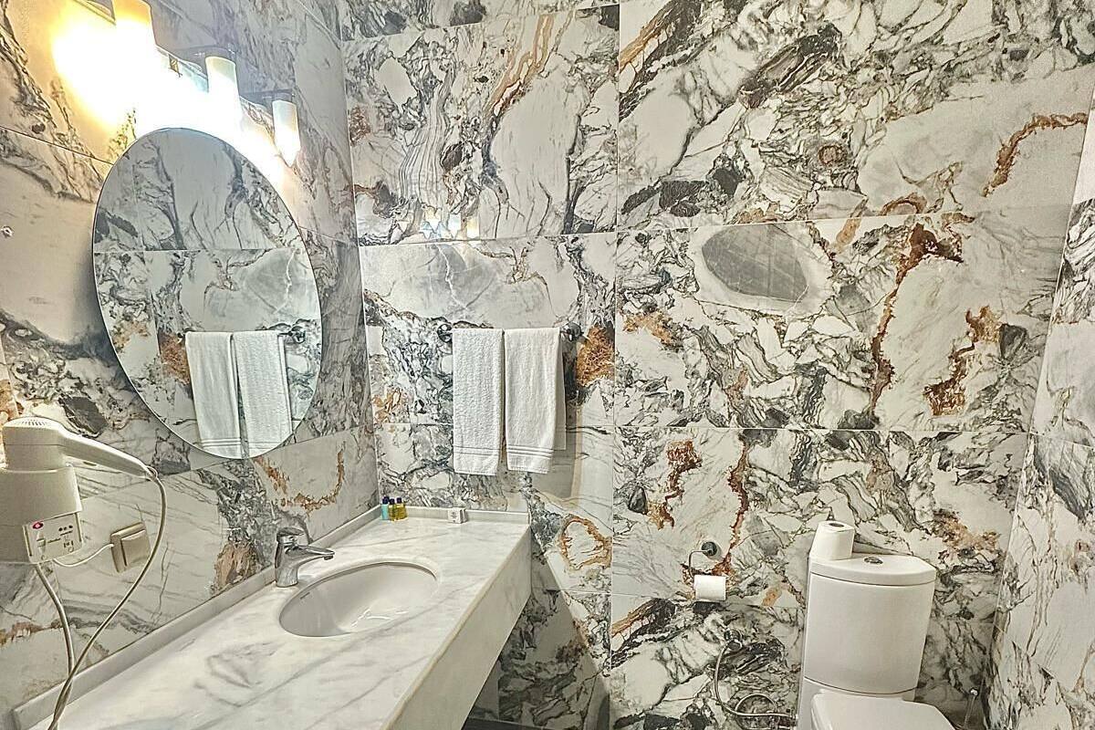 A bathroom with a marble sink, a toilet, and a mirror.