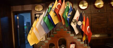 Una exhibición de varias banderas nacionales colgadas de una estructura de madera con placas, en una sala con relojes en la pared.