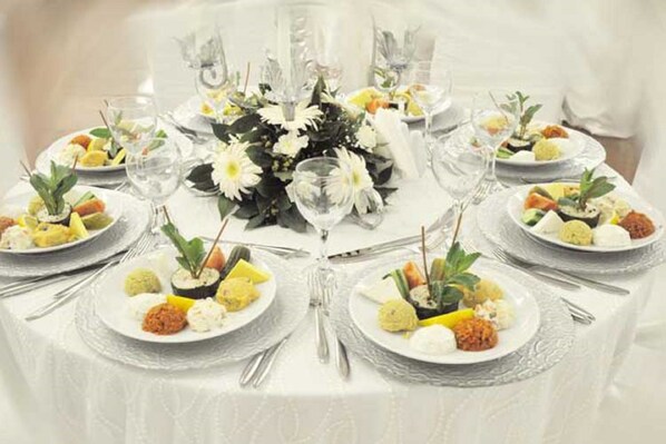 Una mesa de comedor formal dispuesta con varios platos de comida, vasos y cubiertos.