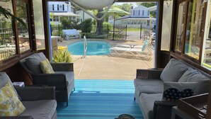 Un área junto a la piscina con muebles de mimbre, una esterilla azul y vistas a una piscina y casas al fondo.
