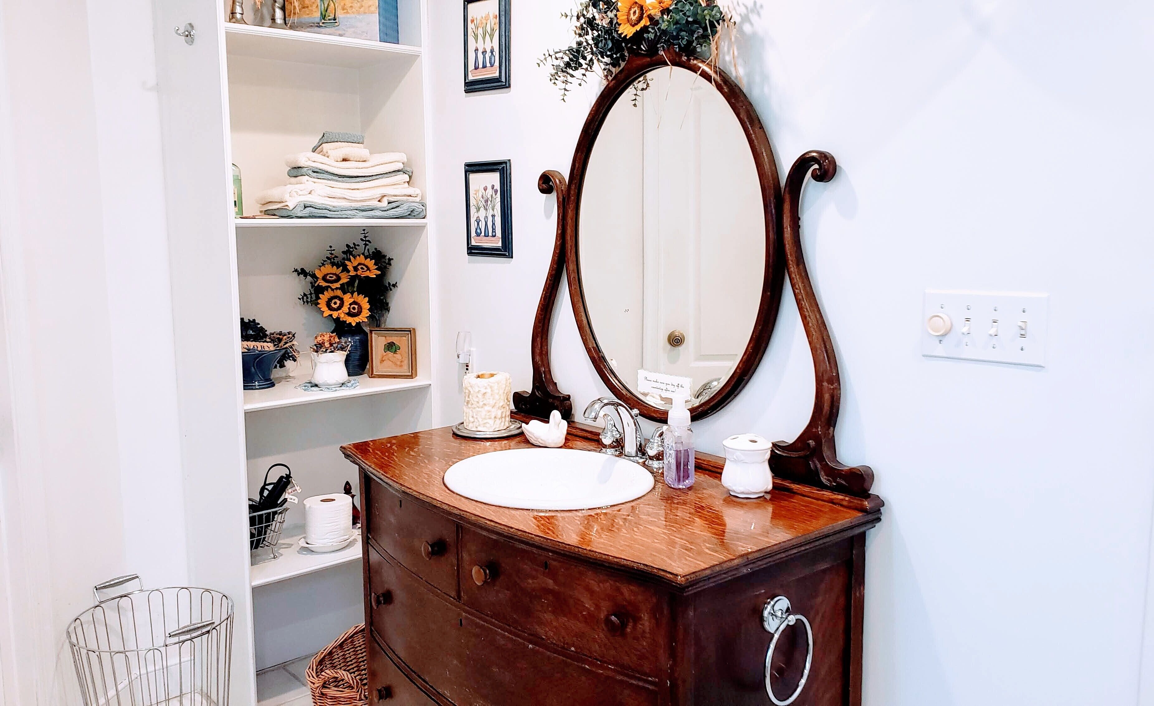 A bathroom with a wooden vanity, a large mirror, and shelves with towels and toiletries.