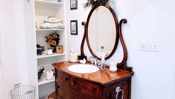 A bathroom with a wooden vanity, a large mirror, and shelves with towels and toiletries.