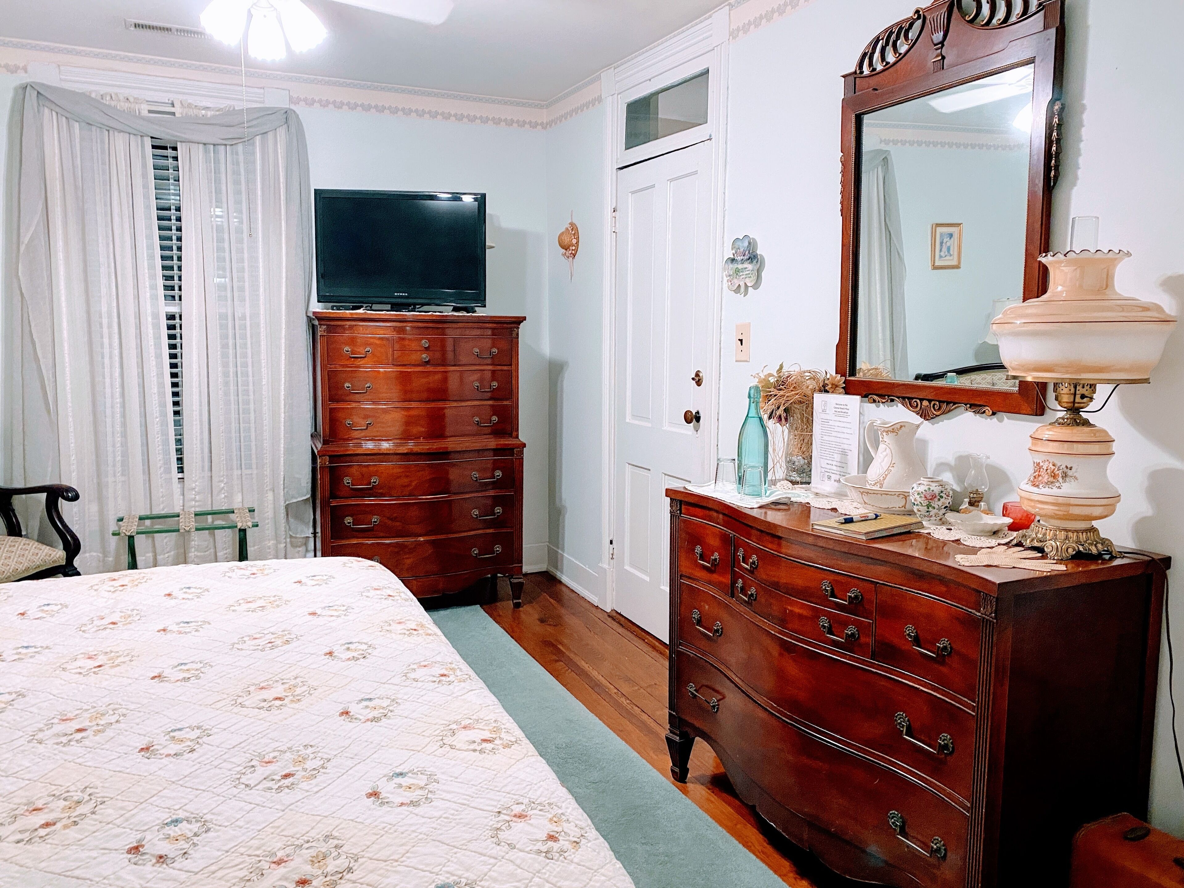 Un dormitorio con una cama, un aparador de madera, un televisor, un espejo y una lámpara.