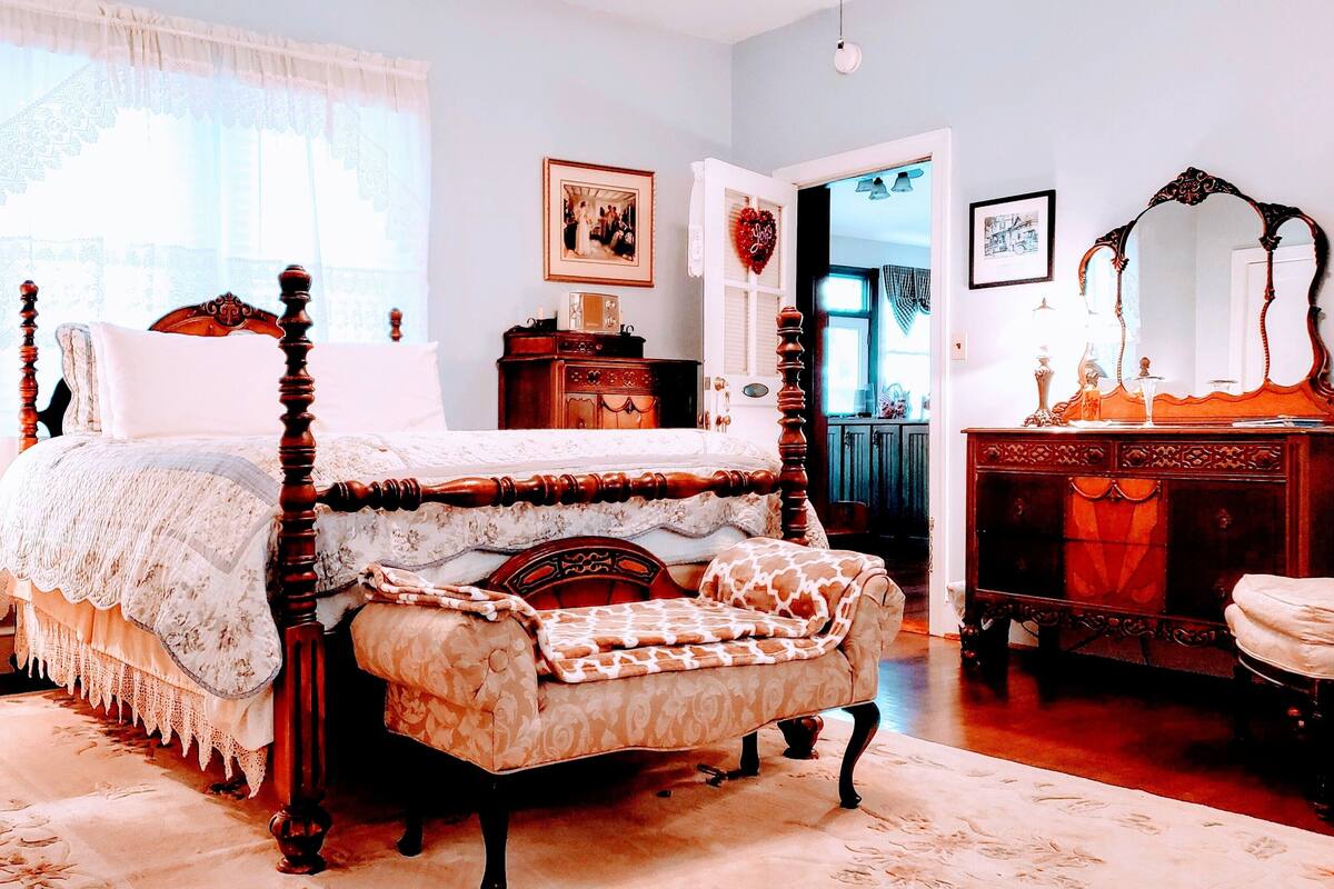 A traditional bedroom with a four-poster bed, a nightstand, a dresser, and a mirror.