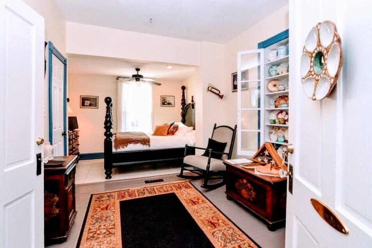 A bedroom with a bed, a chair, a dresser, and a shelf with decorative items.