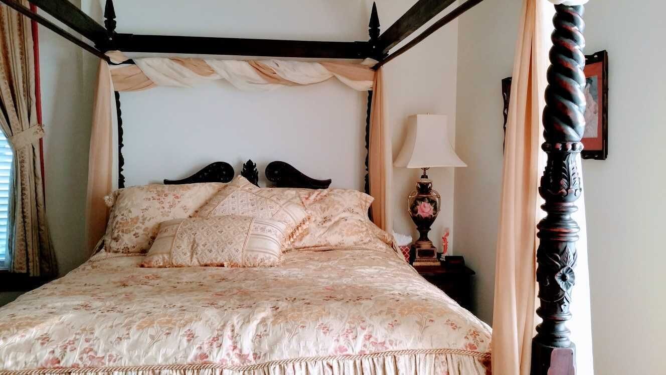 Un lit à baldaquin avec une literie à motifs floraux, une table de chevet avec une lampe et un tableau encadré au mur.