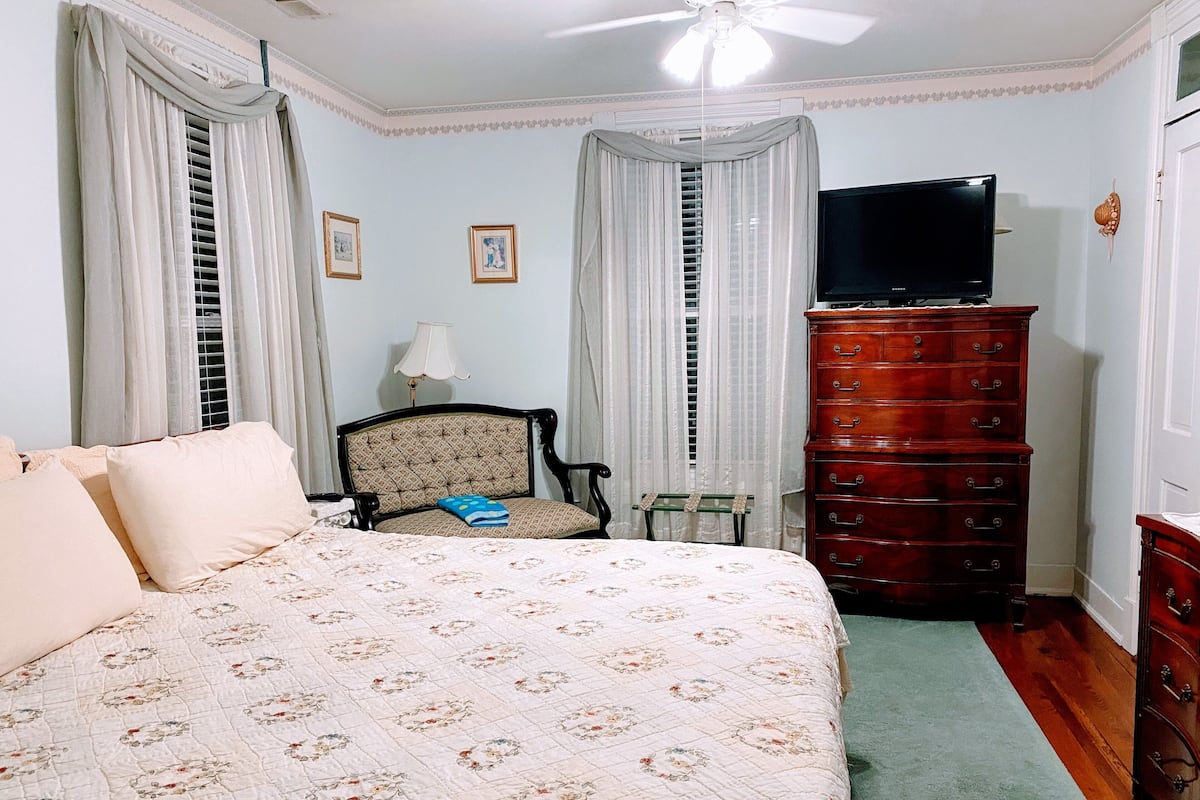 A bedroom with a bed, a dresser, a chair, a television, and a ceiling fan.