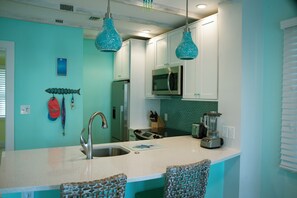 A kitchen with a central island, stainless steel appliances, teal walls, and hanging blue pendant lights.