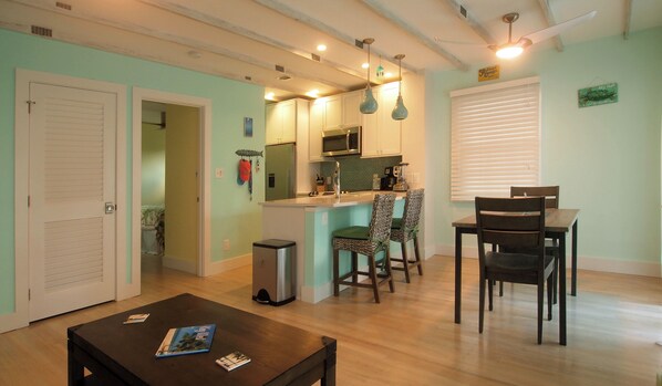 A compact kitchen with a microwave, sink, and a small island. There is a dining area with two chairs and a table.