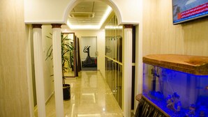 A hallway with marble flooring, white columns, a large aquarium, and a television screen on the wall. - Jubail Inn (Al Jubail)