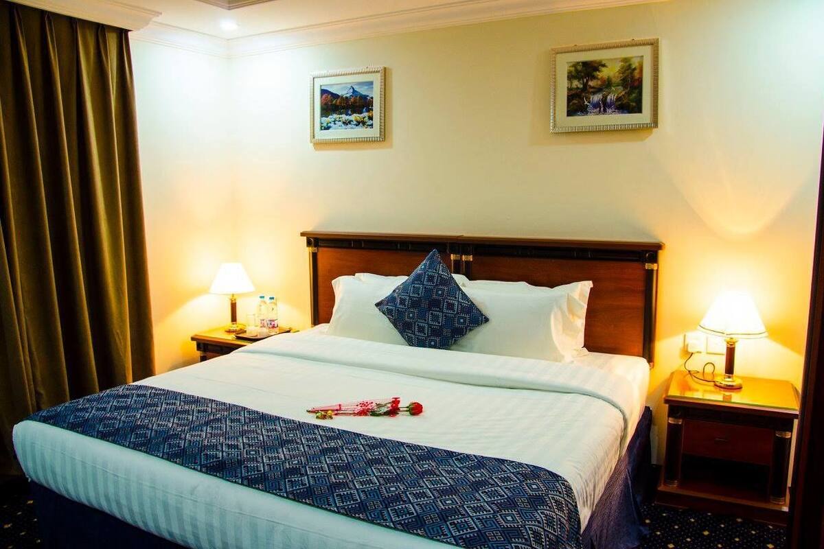 A hotel room with a large bed, two bedside lamps, a wooden headboard, and two framed pictures on the wall.