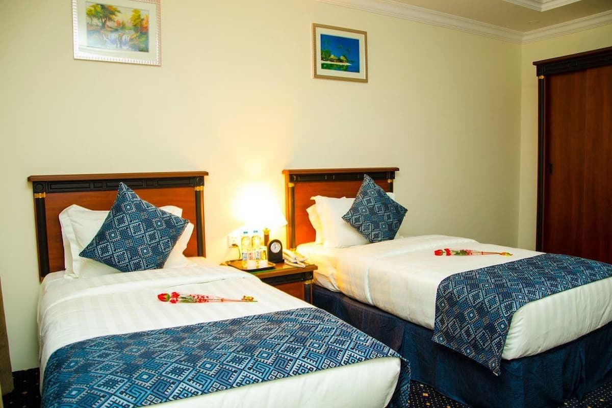 Two single beds with matching headboards and footboards, a bedside table with a lamp, and a wall-mounted clock.