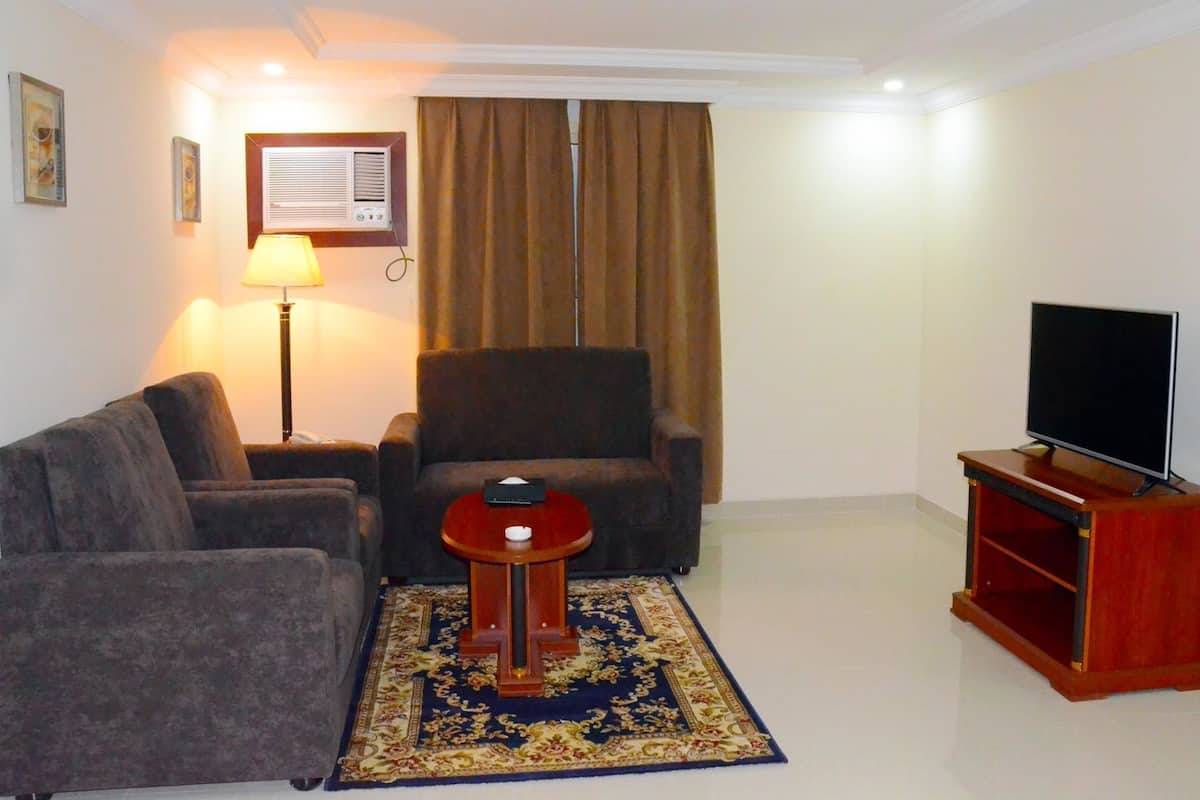 A living room with a sofa, armchair, TV stand, and a decorative rug.