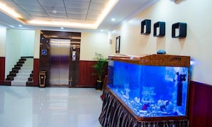 A hotel lobby with a reception desk, a large aquarium, a staircase, and an elevator. - Jubail Inn (Al Jubail)