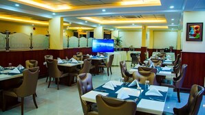 A restaurant with multiple dining tables and chairs, a television screen, and a decorative wall. - Jubail Inn (Al Jubail)