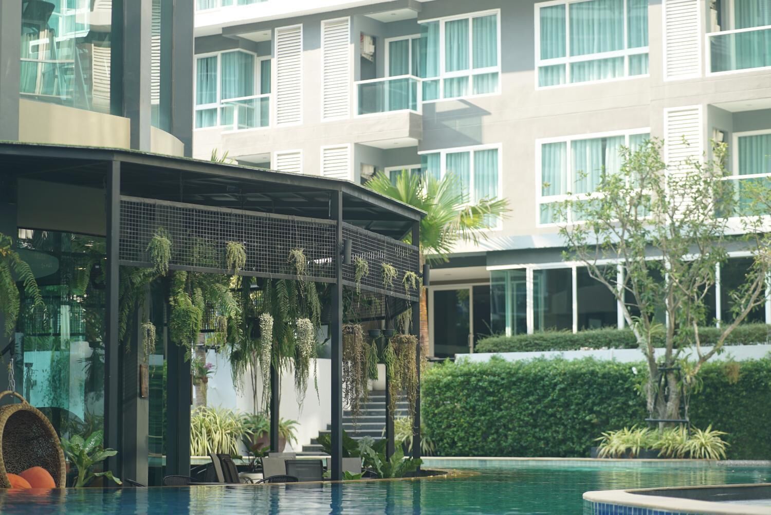 A modern hotel with a pool area, indoor plants, and a covered seating area.