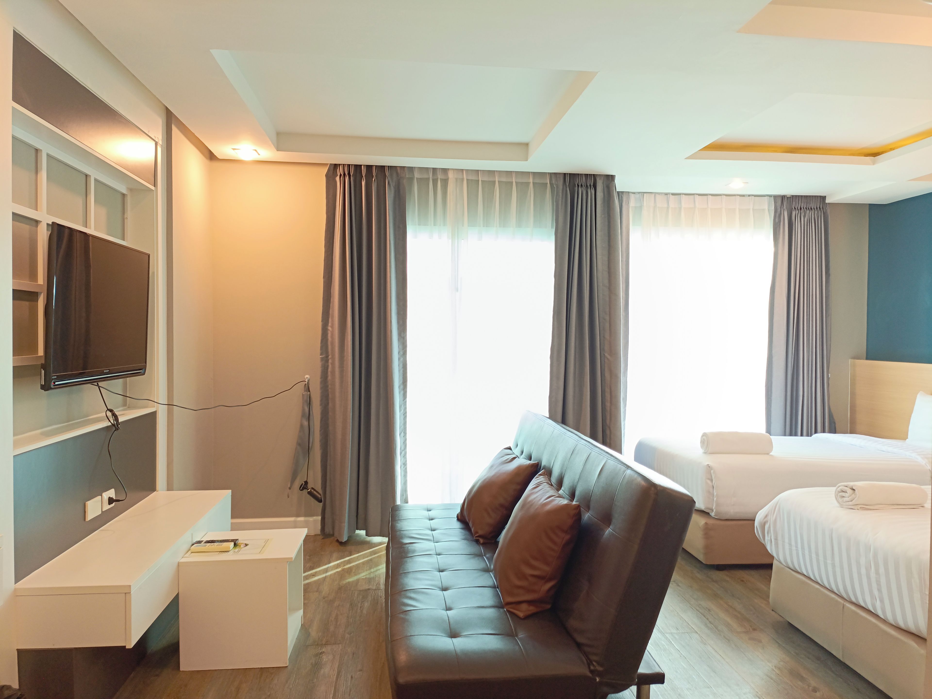 A hotel room with a sofa, a bed, a desk, and a TV mounted on the wall.