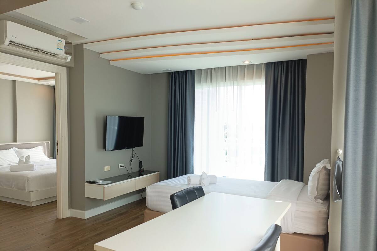 A modern hotel room with a bed, a desk, a TV, and a window with curtains.