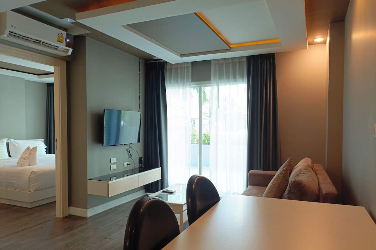 A modern hotel room with a bed, a TV mounted on the wall, a dining area with a table and chairs, and a sofa.