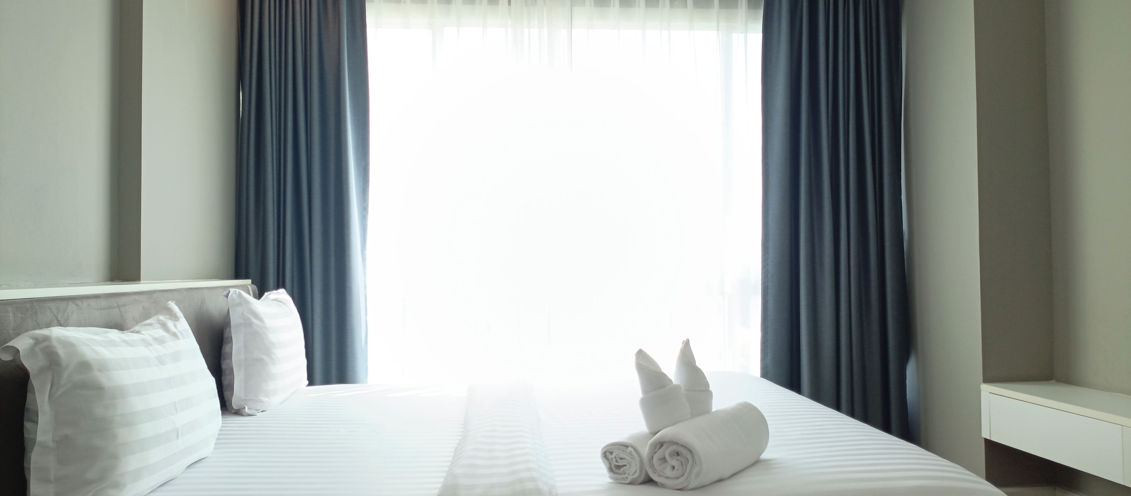 Una habitación de hotel con una cama bien hecha, dos almohadas y un par de toallas enrolladas sobre la cama.