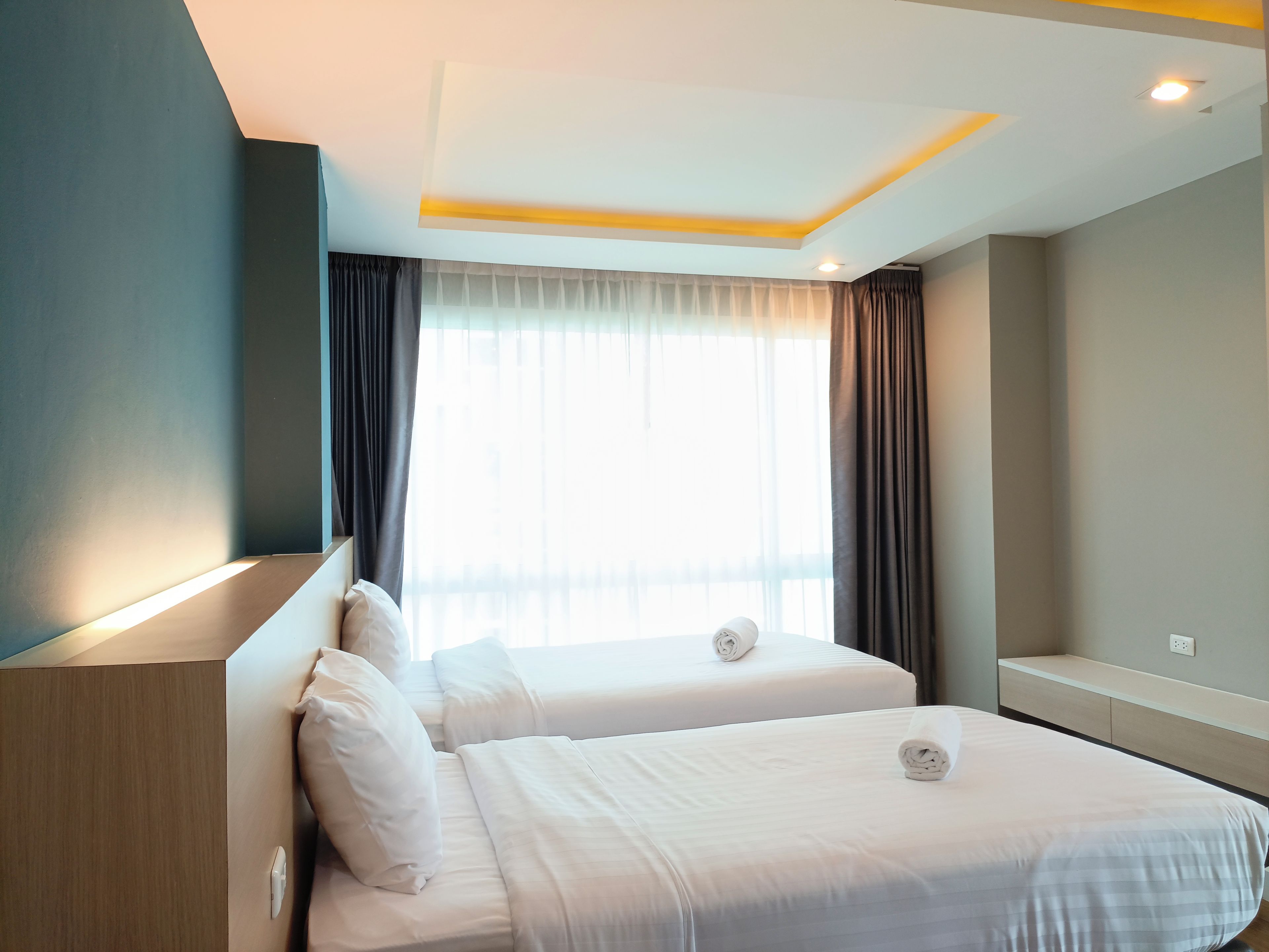 A hotel room with two beds, a large window with curtains, and a modern ceiling design.