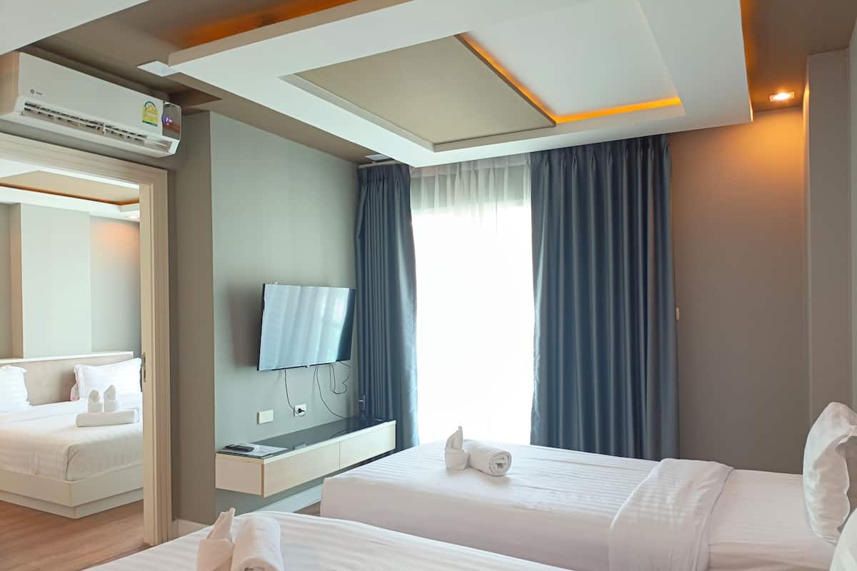 A hotel room with two beds, a flat-screen TV mounted on the wall, a desk with a chair, and a window with curtains.