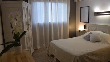 A bedroom with a bed, a nightstand, a lamp, a potted orchid, and a window with curtains.