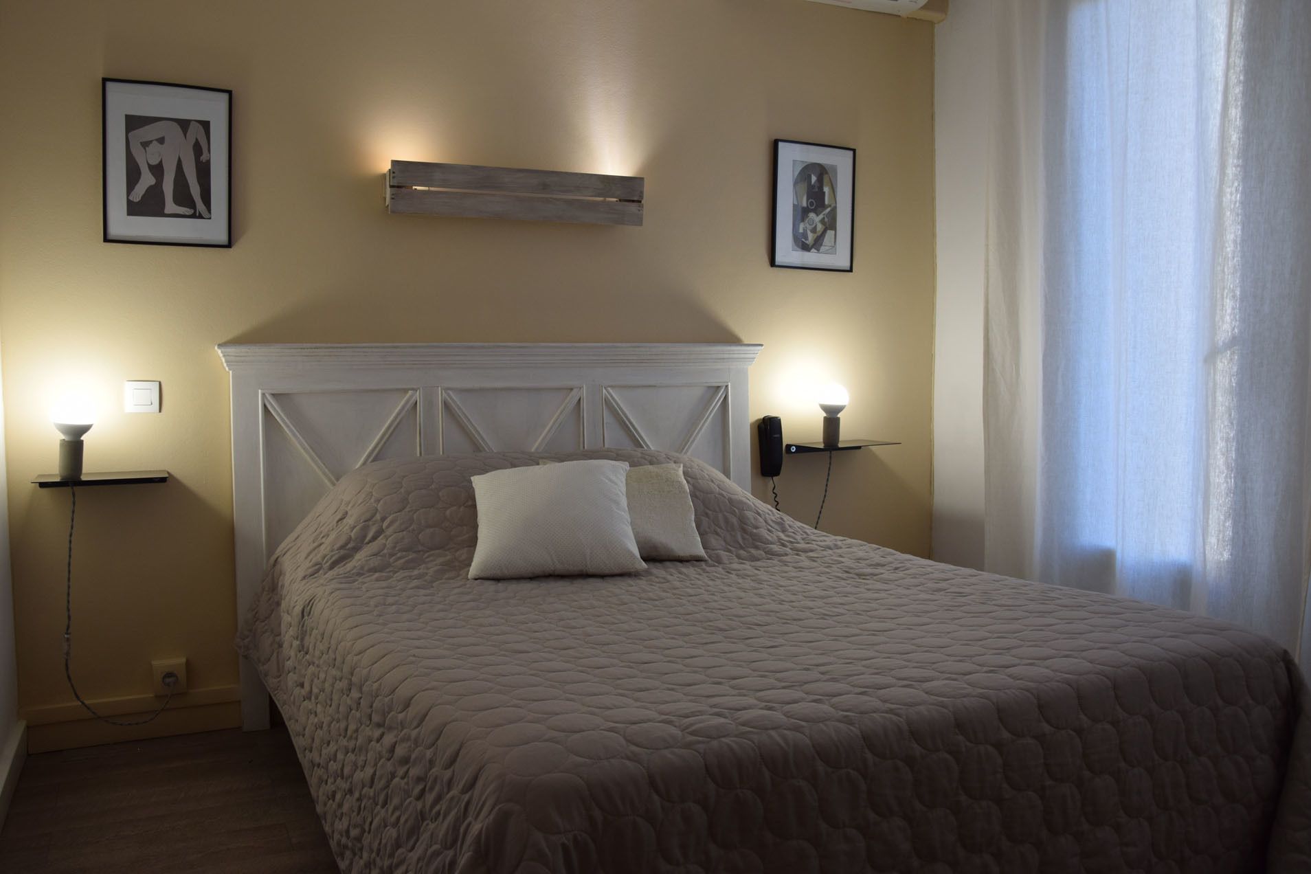Een slaapkamer met een bed, twee bedlampjes en twee foto’s in lijsten aan de muur.
