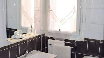 Une salle de bain avec un lavabo blanc, des toilettes et une fenêtre ornée de rideaux légers.