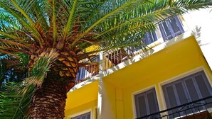 A yellow building with balconies and shutters, surrounded by palm trees. - Hôtel Le Grillon (L'Île-Rousse)