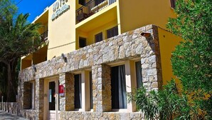 A hotel with a yellow facade, stone lower section, and balconies. - Hôtel Le Grillon (L'Île-Rousse)