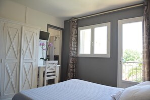 A bedroom with a bed, a desk with a chair, a mirror, and a window with shutters.