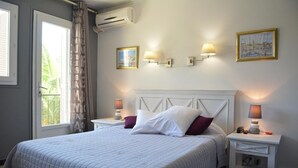 A neatly arranged bedroom with a large bed, two bedside tables with lamps, a headboard, and a window with curtains. - Hôtel Le Grillon (L'Île-Rousse)