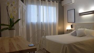 Ein Hotelzimmer mit Bett, Schreibtisch, Stuhl, einer Zimmerpflanze und einem Vorhangfenster.