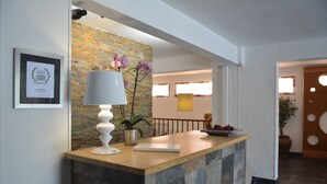 A reception desk with a framed award, a potted plant, and a lamp. - Hôtel Le Grillon (L'Île-Rousse)