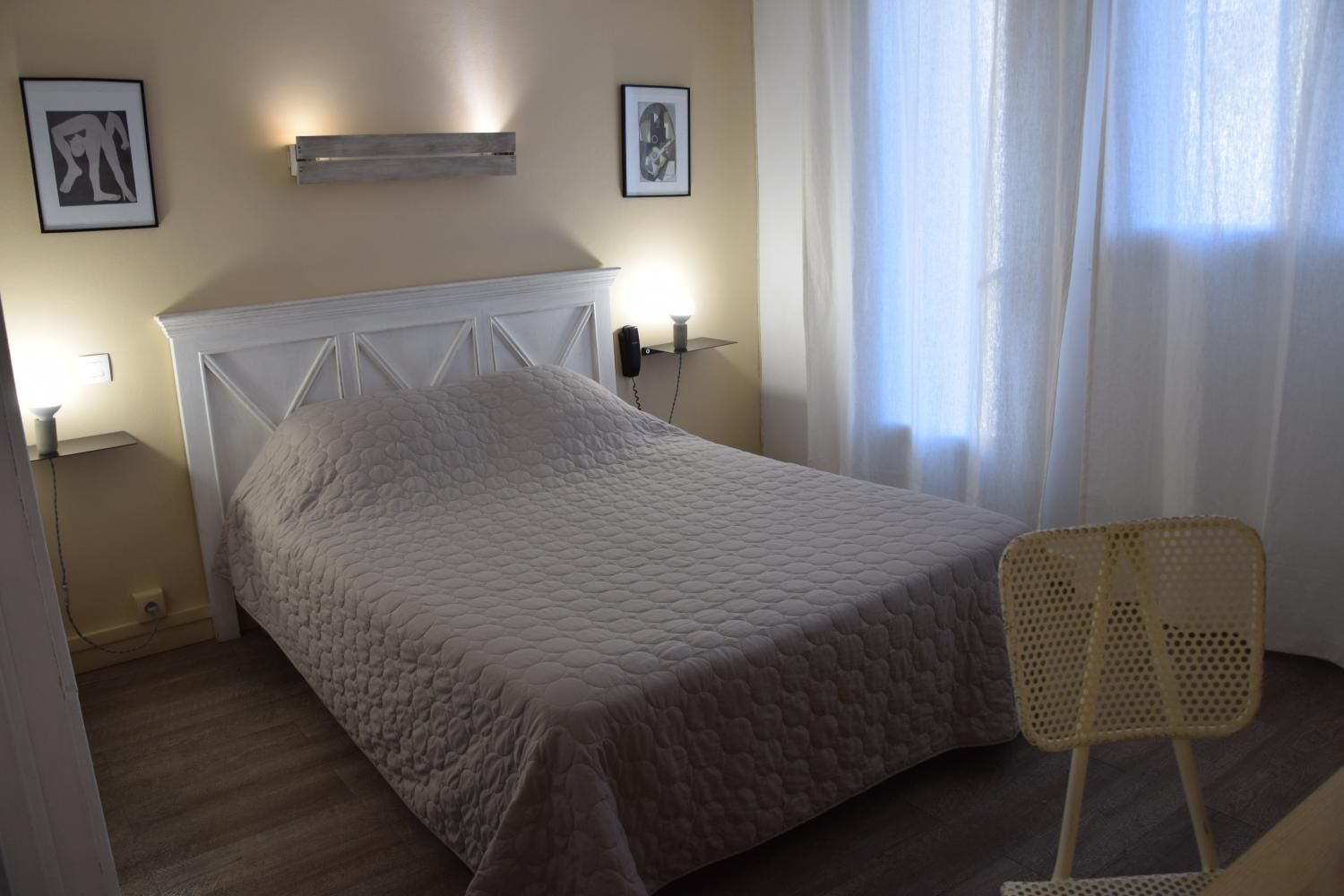A bedroom with a bed, a chair, and two wall-mounted lamps.