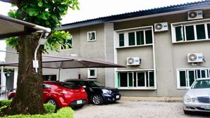 Un bâtiment doté de plusieurs unités de climatisation, d’un espace de stationnement couvert et d’un arbre au premier plan.